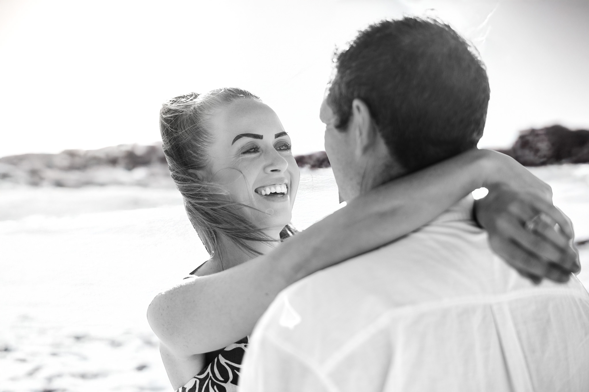 Black and white portrait of a woman laughing while embracing her partner on the beach