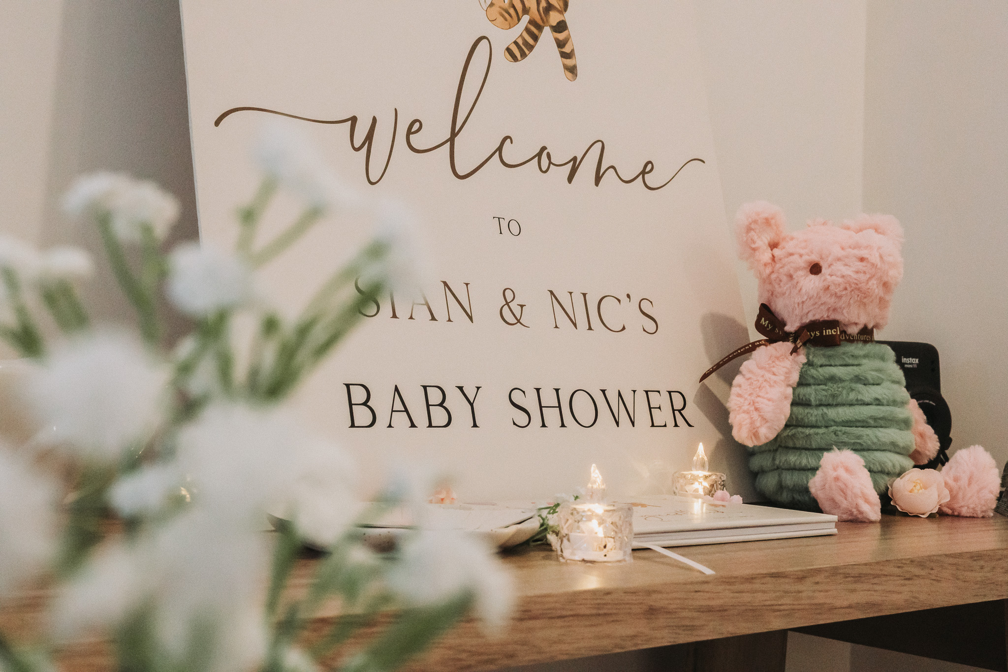 Cream welcome sign for Sian and Nic's baby shower beside a pink teddy and candlelight