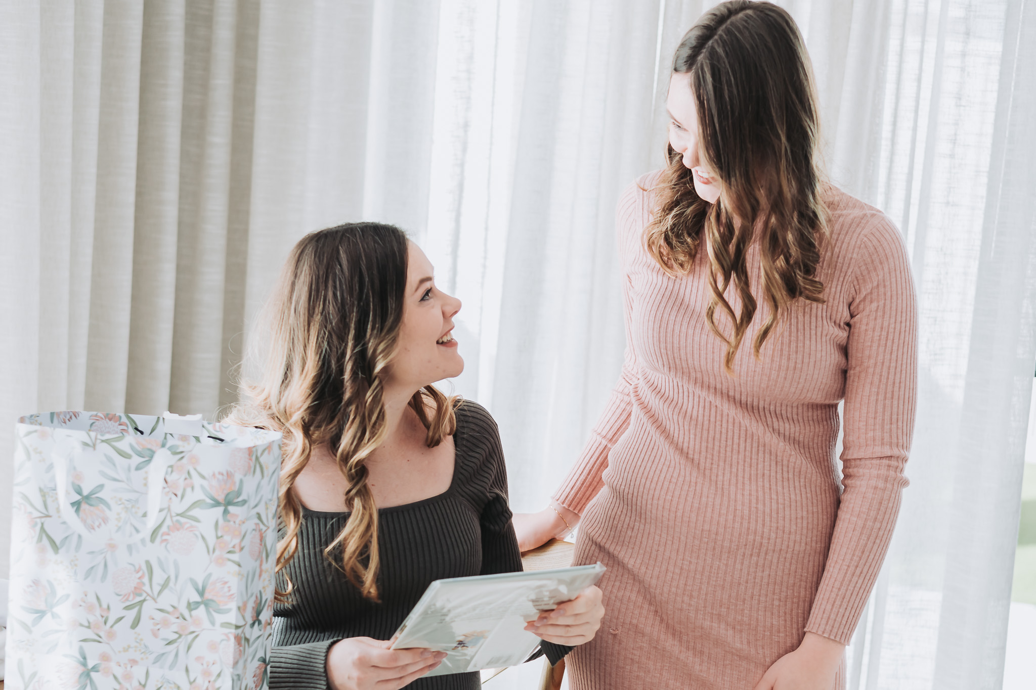 Two friends sharing a joyful gift moment by a bright window at a Perth celebration