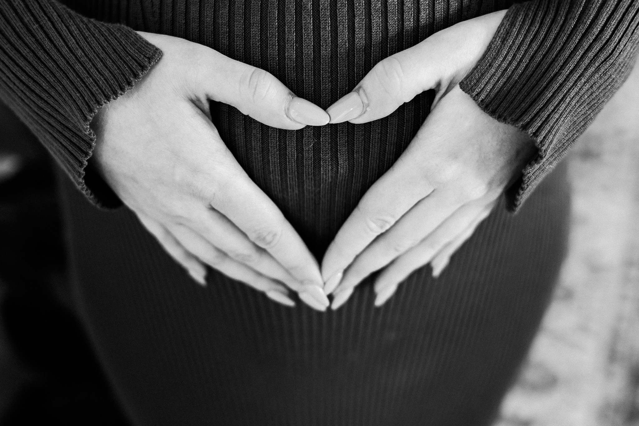 Black and white detail of hands forming a heart over a pregnant belly in a ribbed dress